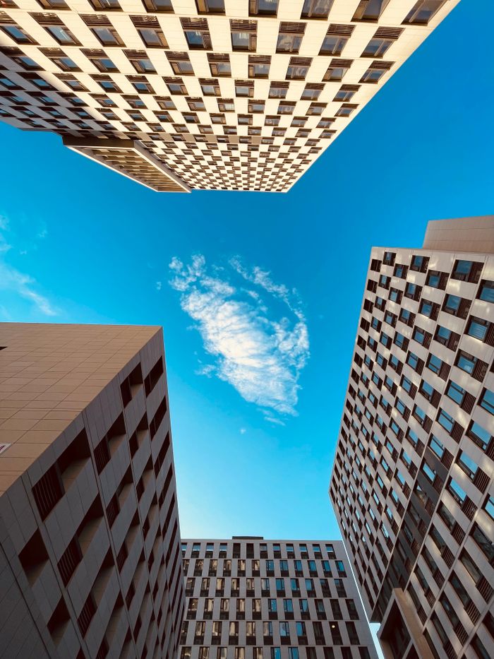 Perspective view of high-rise buildings framing a blue sky with clouds.